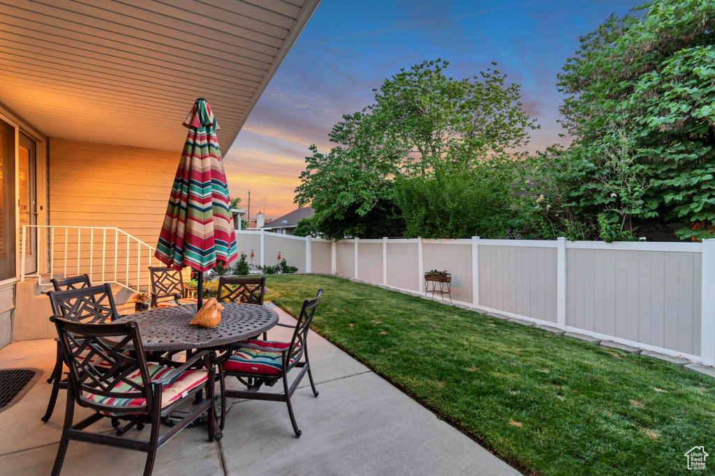 Patio terrace at dusk with a fenced backyard, outdoor dining area, and a patio area