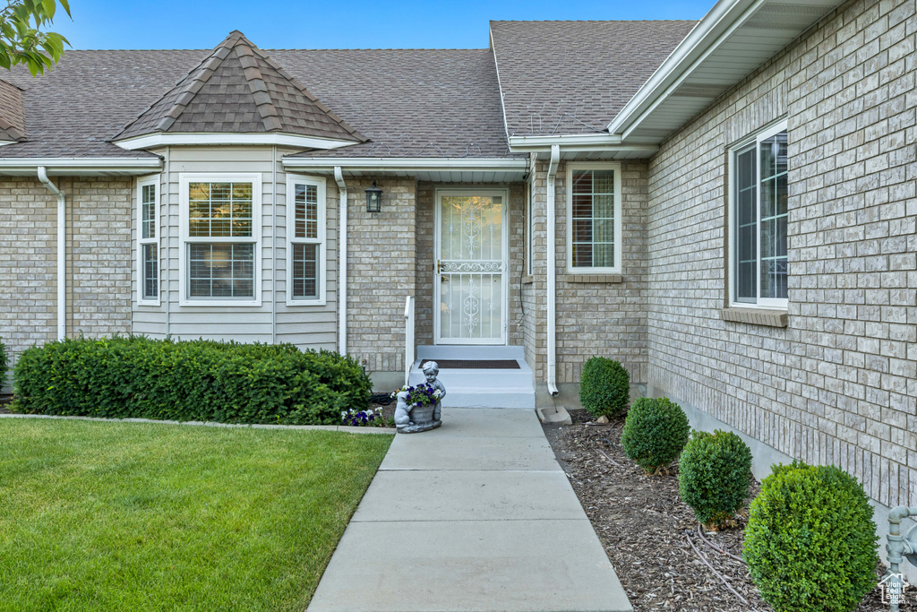 Property entrance with a yard, a shingled roof, and brick siding