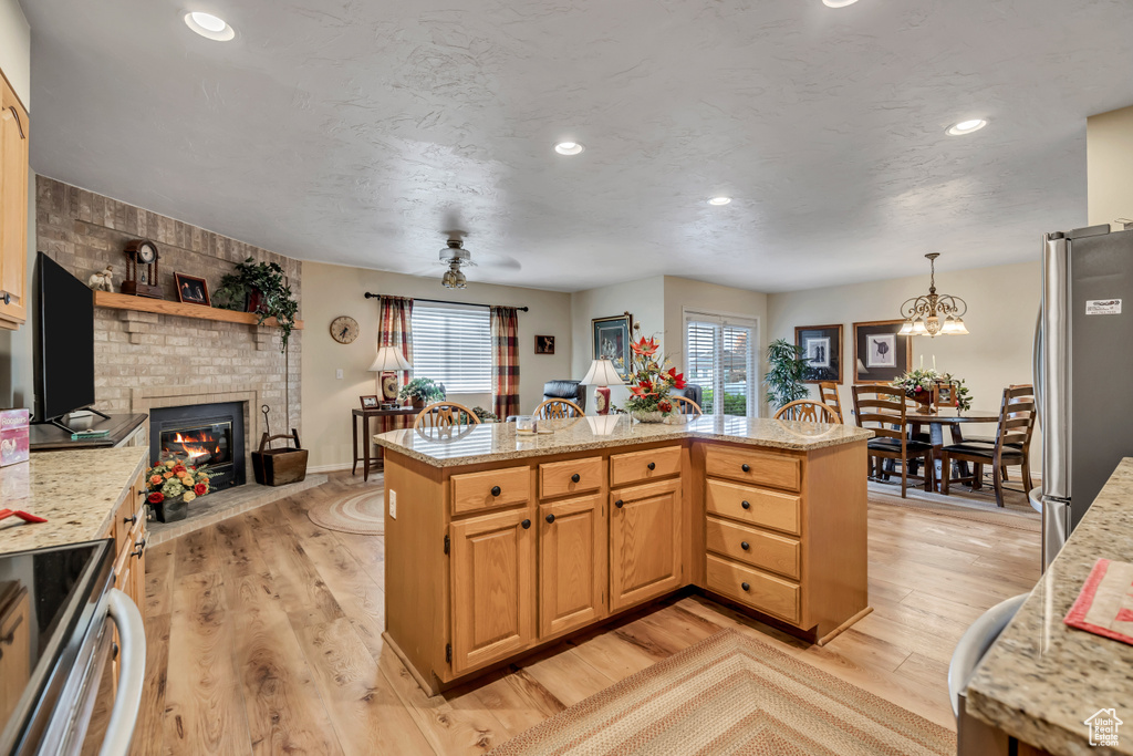 Kitchen featuring appliances with stainless steel finishes, light wood-style floors, a fireplace, light stone counters, and recessed lighting