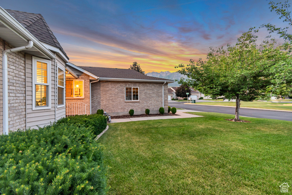View of property exterior with brick siding, a yard, and roof with shingles