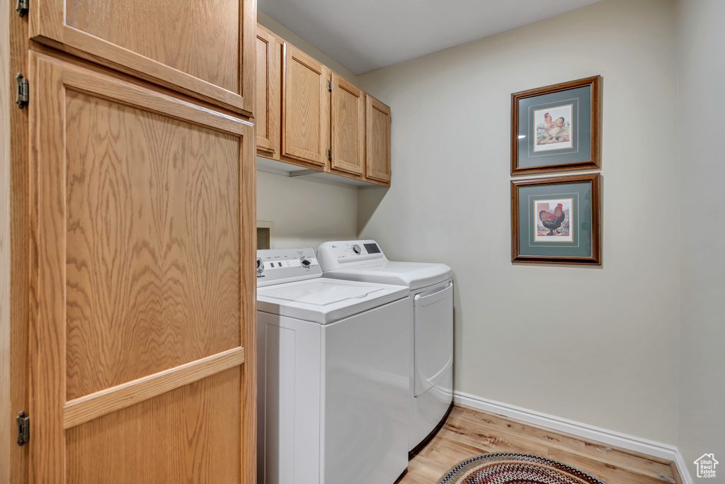 Laundry room featuring washer and clothes dryer, light wood-type flooring, and cabinet space