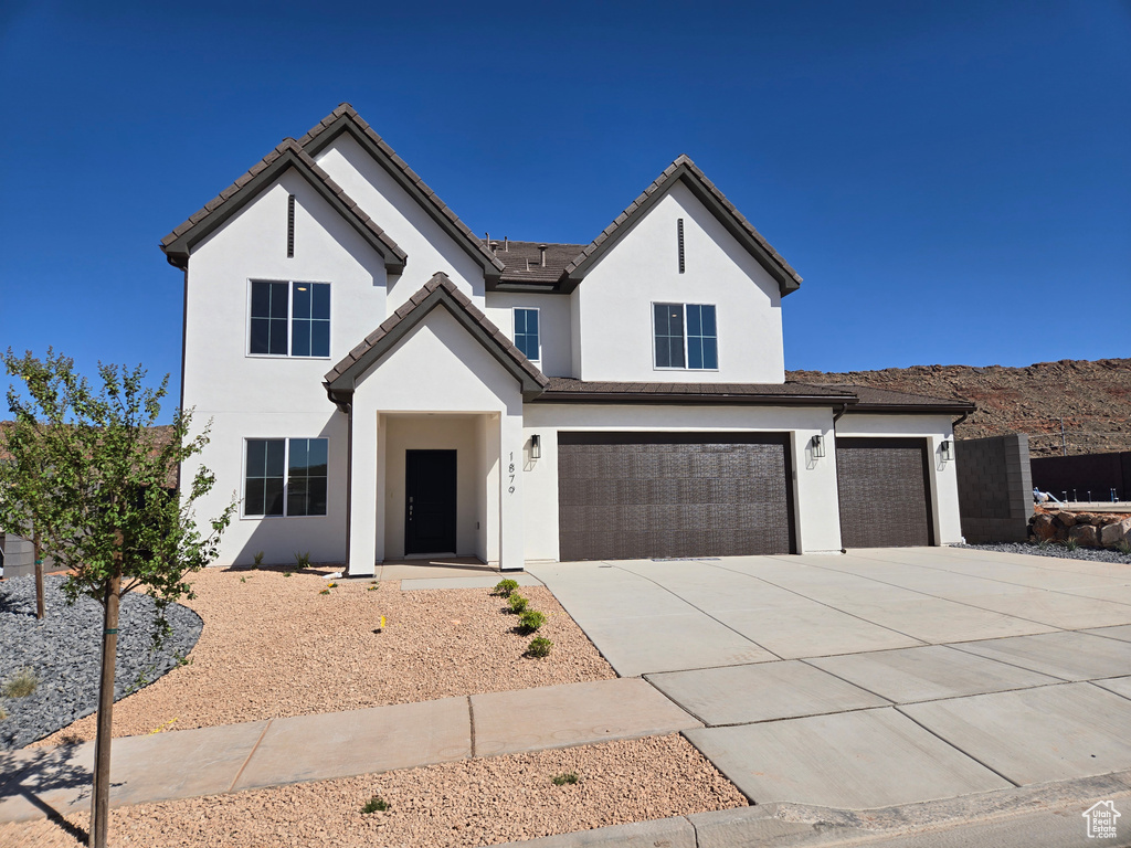 View of front of property featuring driveway, stucco siding, an attached garage, and a tiled roof