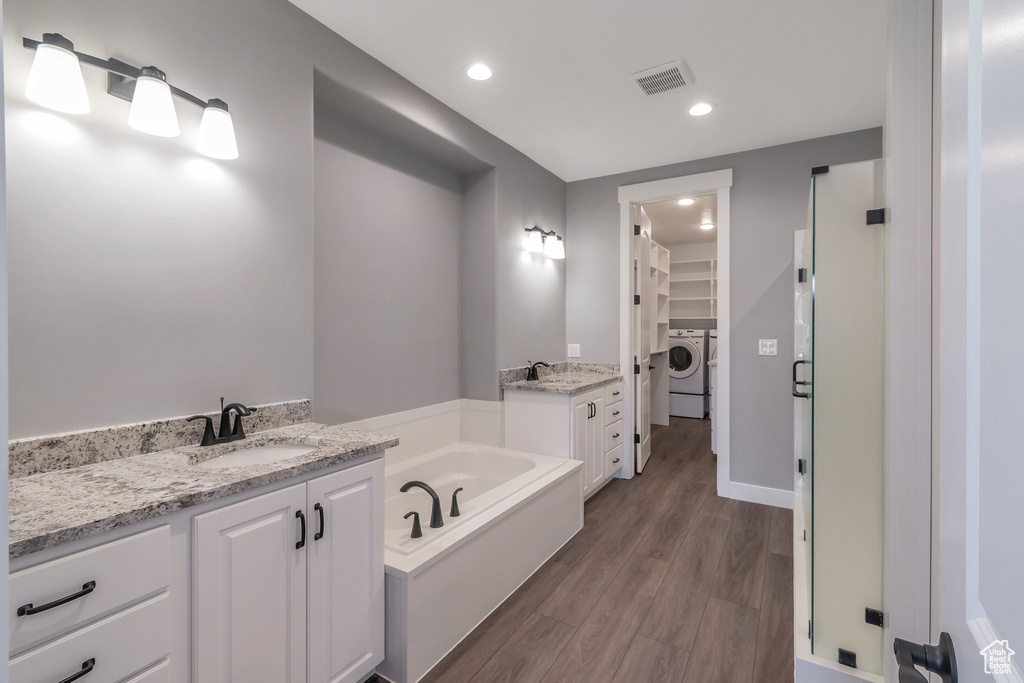 Bathroom with washer / dryer, a walk in closet, vanity, a bath, and wood finished floors