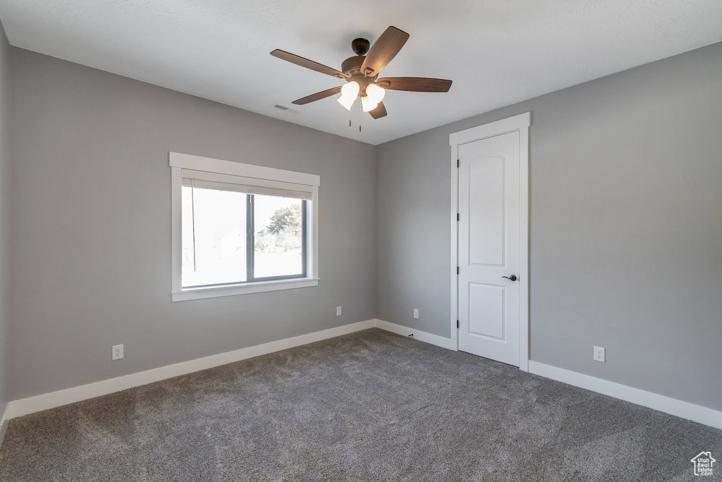 Spare room featuring dark colored carpet and ceiling fan