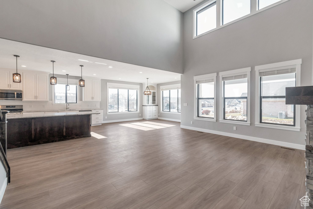 Unfurnished living room featuring wood finished floors, healthy amount of natural light, recessed lighting, and a high ceiling