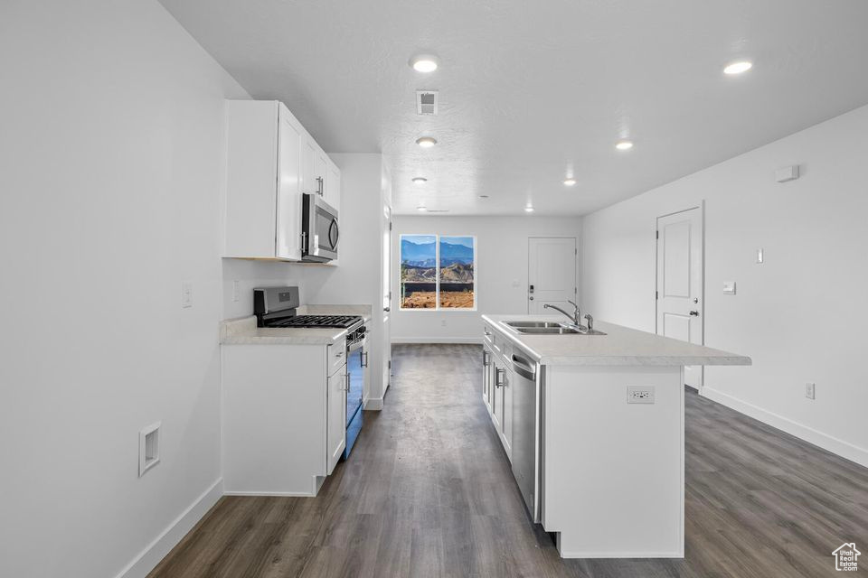 Kitchen featuring stainless steel appliances, an island with sink, white cabinets, light countertops, and dark wood finished floors
