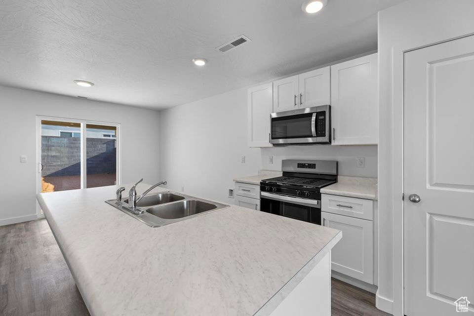 Kitchen with appliances with stainless steel finishes, dark wood finished floors, white cabinets, recessed lighting, and an island with sink