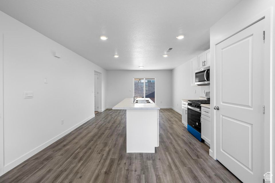 Kitchen featuring appliances with stainless steel finishes, white cabinetry, recessed lighting, dark wood-type flooring, and an island with sink