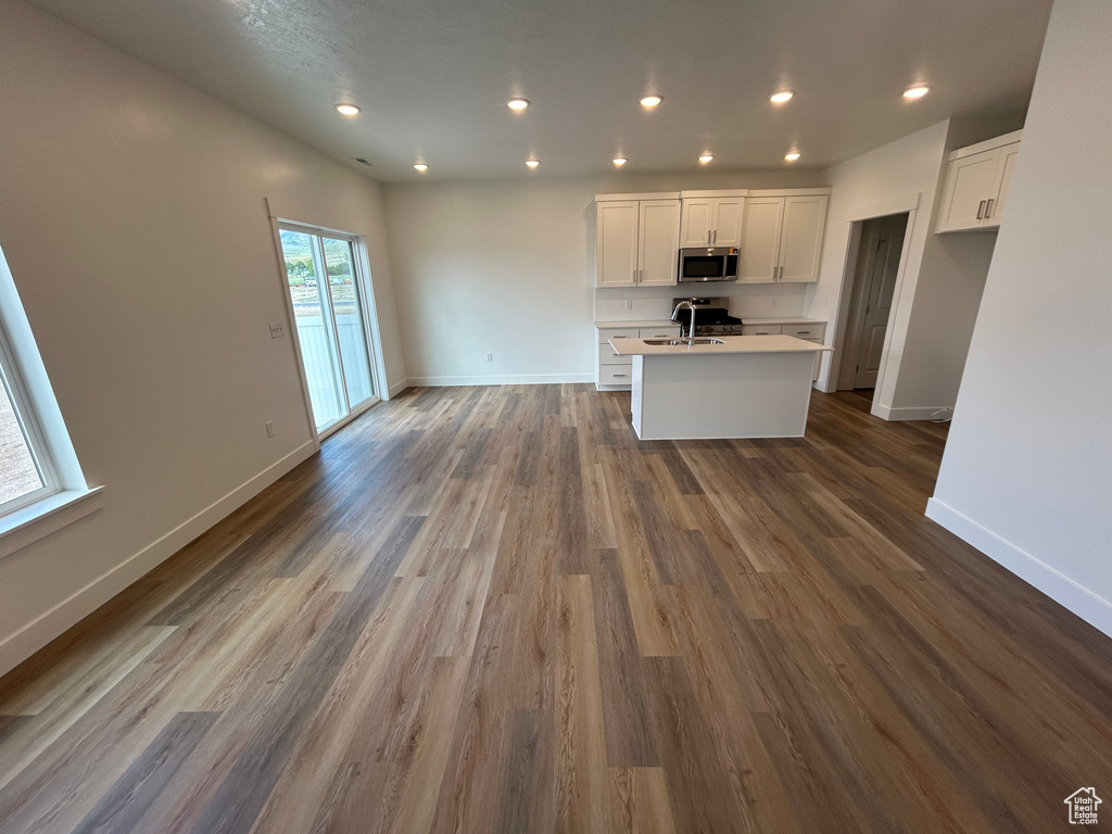 Kitchen featuring stainless steel microwave, a center island with sink, white cabinets, open floor plan, and recessed lighting