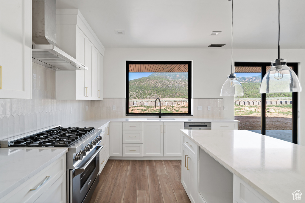 Kitchen with high end stainless steel range oven, wall chimney range hood, light wood-type flooring, and white cabinetry