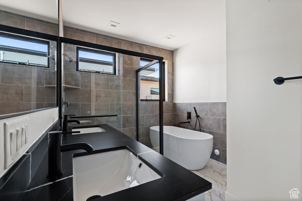 Full bathroom featuring tile walls, a soaking tub, marble finish flooring, and double vanity