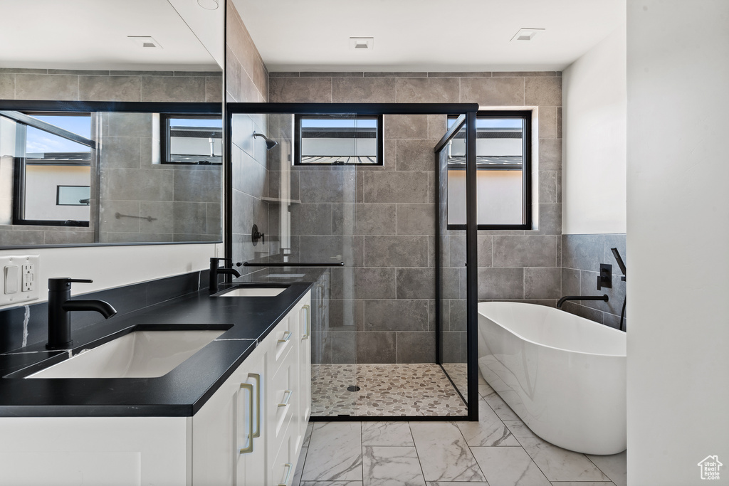 Full bath with tile walls, healthy amount of natural light, a freestanding tub, a stall shower, and marble look tiles