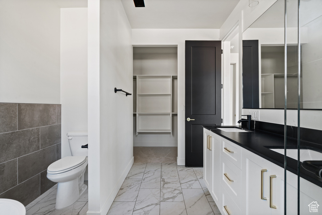 Full bathroom featuring marble look tiles, double vanity, and tile walls