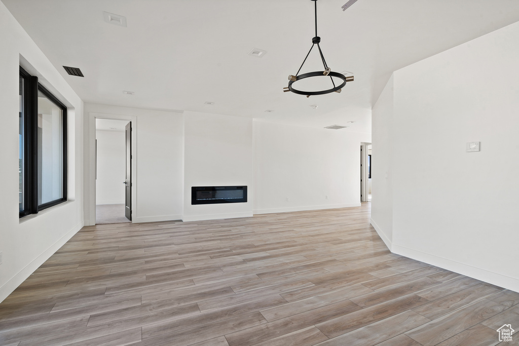 Unfurnished living room featuring light wood finished floors, a glass covered fireplace, and a chandelier