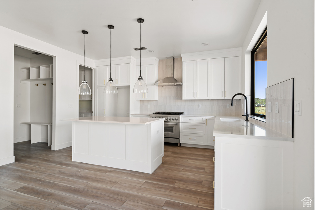 Kitchen with wall chimney exhaust hood, high end range, decorative backsplash, white cabinetry, and light wood finished floors