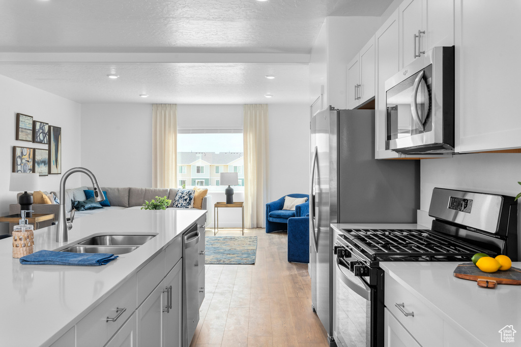 Kitchen with appliances with stainless steel finishes, open floor plan, light countertops, light wood finished floors, and recessed lighting