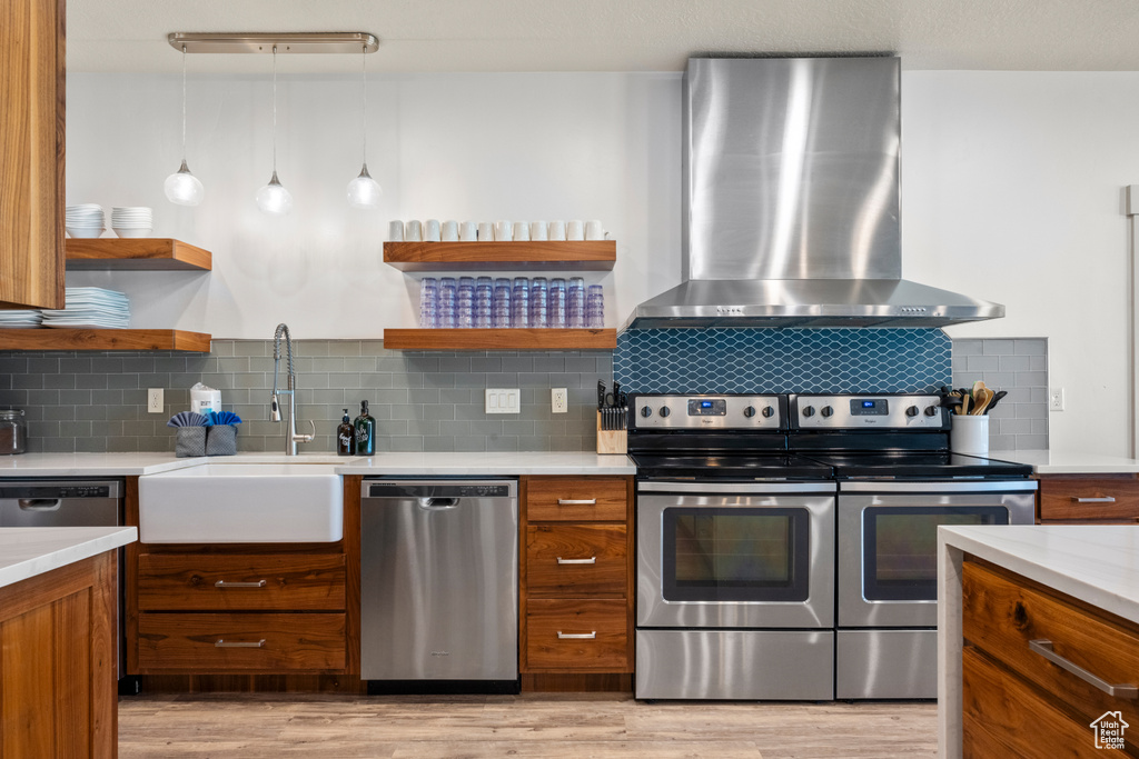 Kitchen with stainless steel appliances, wall chimney range hood, open shelves, and brown cabinets