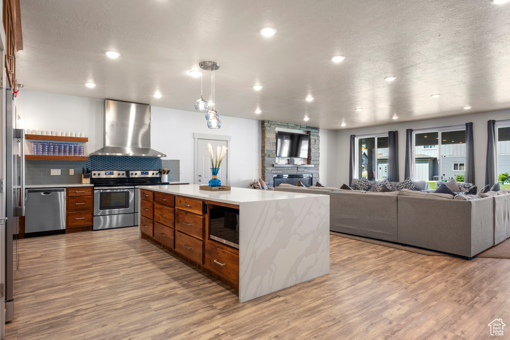 Kitchen featuring ventilation hood, stainless steel appliances, brown cabinetry, light countertops, and recessed lighting