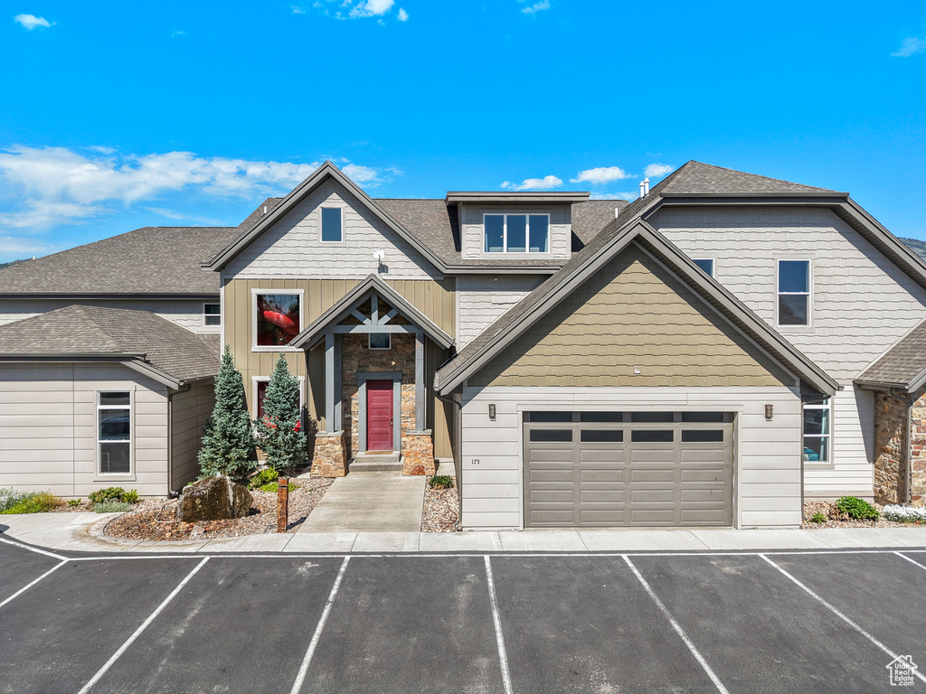 View of front of house with stone siding, a shingled roof, a garage, and asphalt driveway