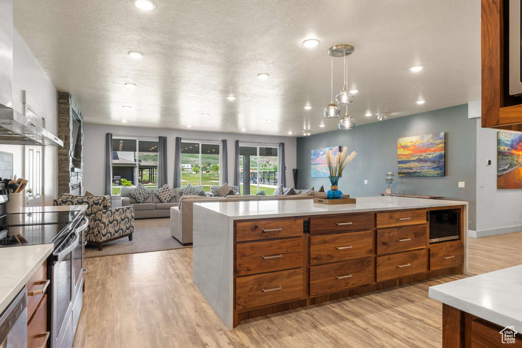 Kitchen featuring brown cabinetry, light wood-style flooring, appliances with stainless steel finishes, light countertops, and open floor plan