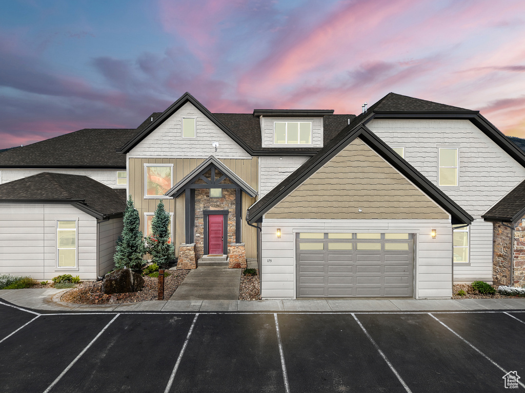 View of front of home with stone siding, asphalt driveway, roof with shingles, and an attached garage