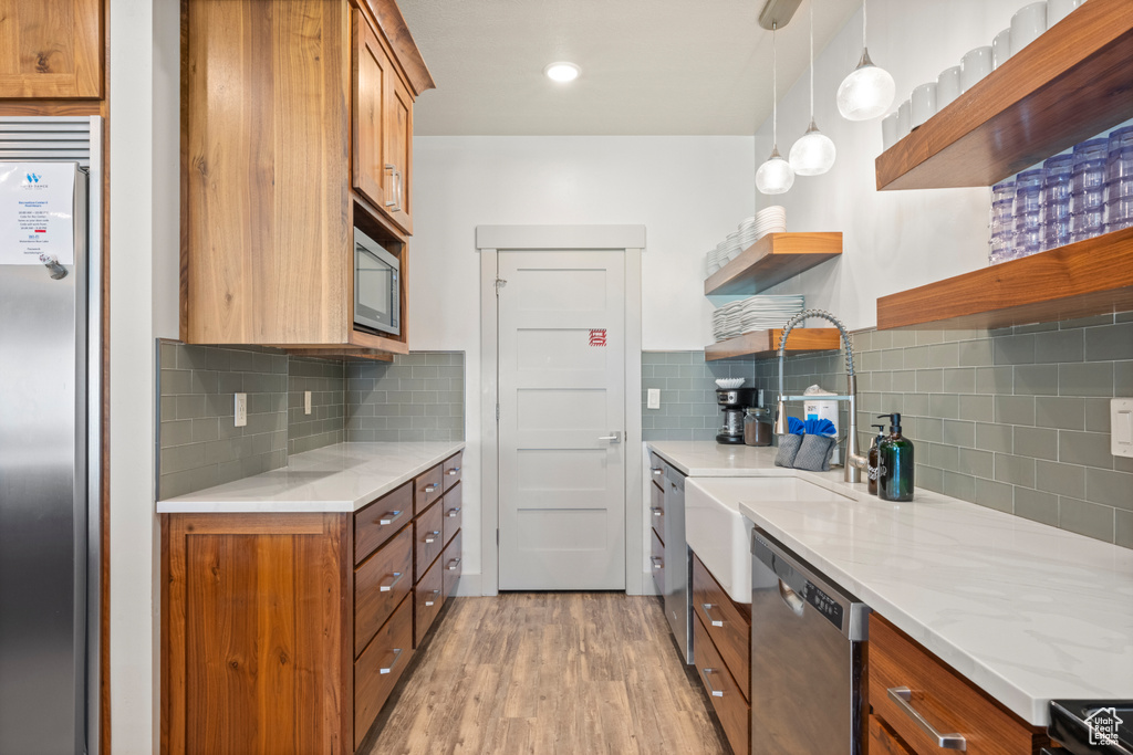 Kitchen featuring open shelves, appliances with stainless steel finishes, brown cabinets, light wood finished floors, and tasteful backsplash