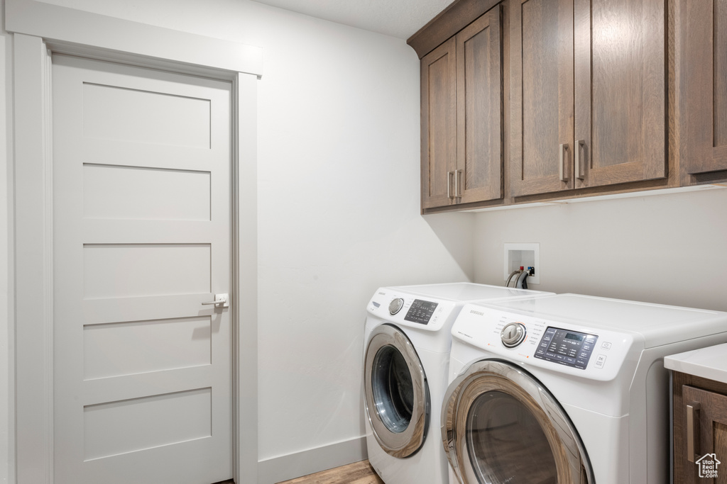 Washroom featuring cabinet space, washer and clothes dryer, and light wood finished floors