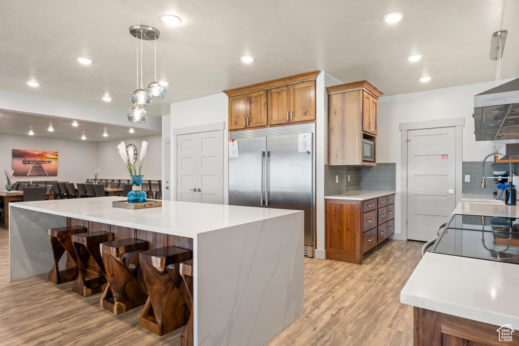 Kitchen featuring built in fridge, light wood-style floors, brown cabinets, decorative backsplash, and recessed lighting