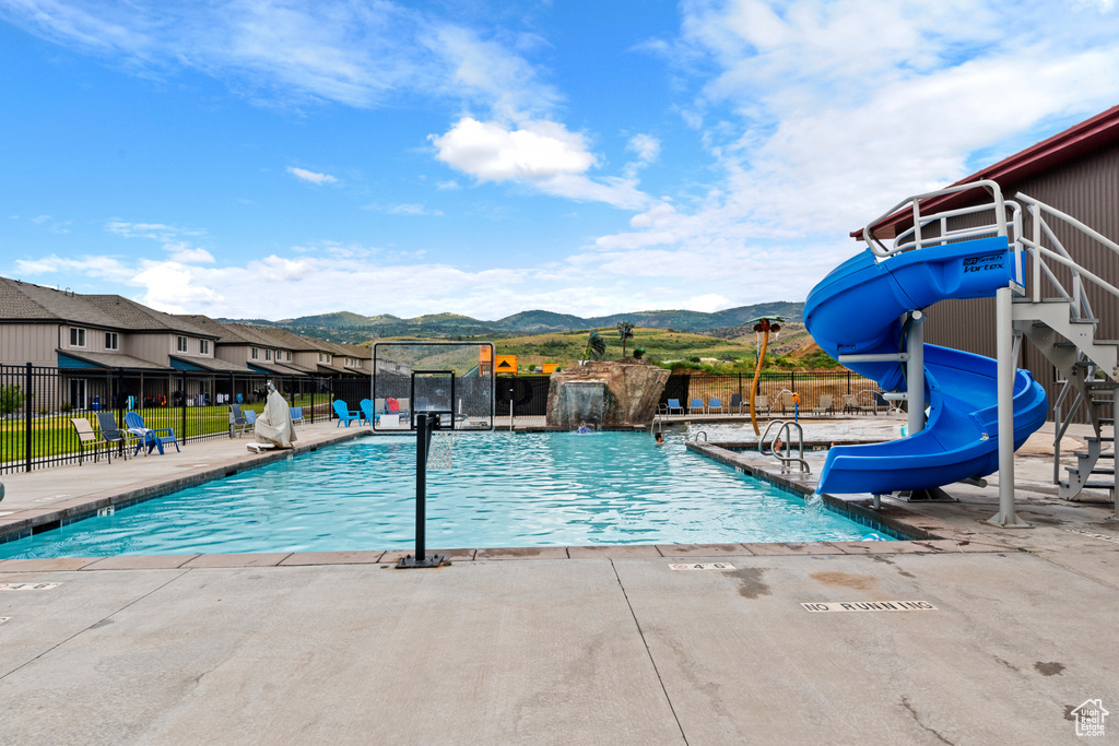 Community pool featuring a water slide, a mountain view, and a patio