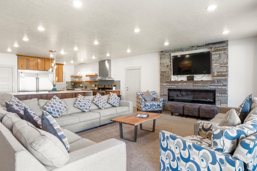 Living room featuring recessed lighting, carpet, a stone fireplace, and a textured ceiling