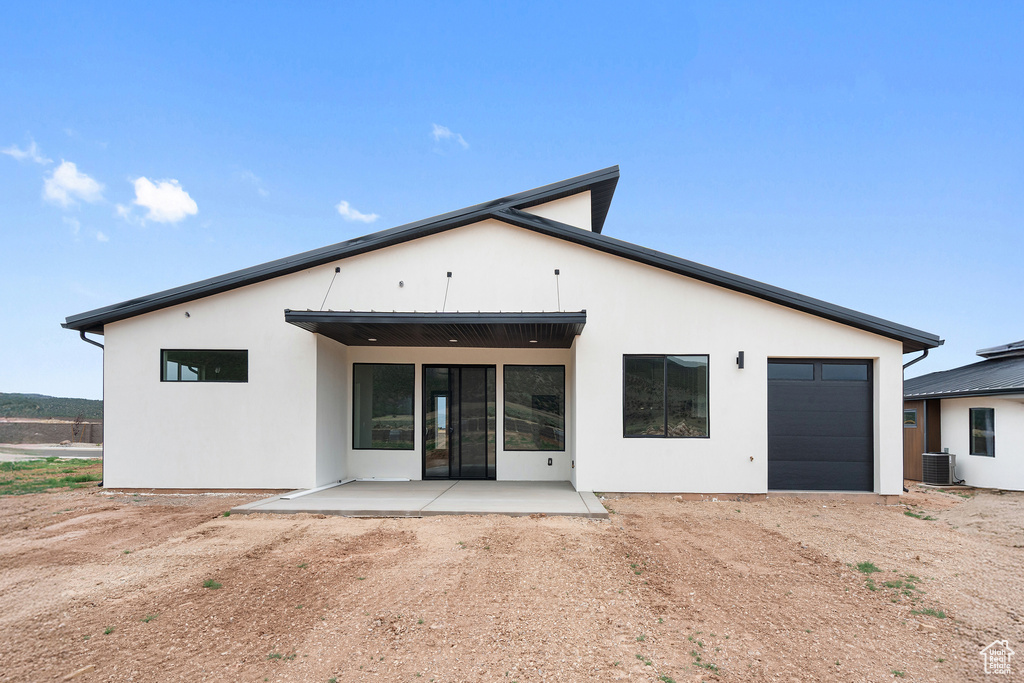 Rear view of house with a garage, dirt driveway, a patio area, and stucco siding