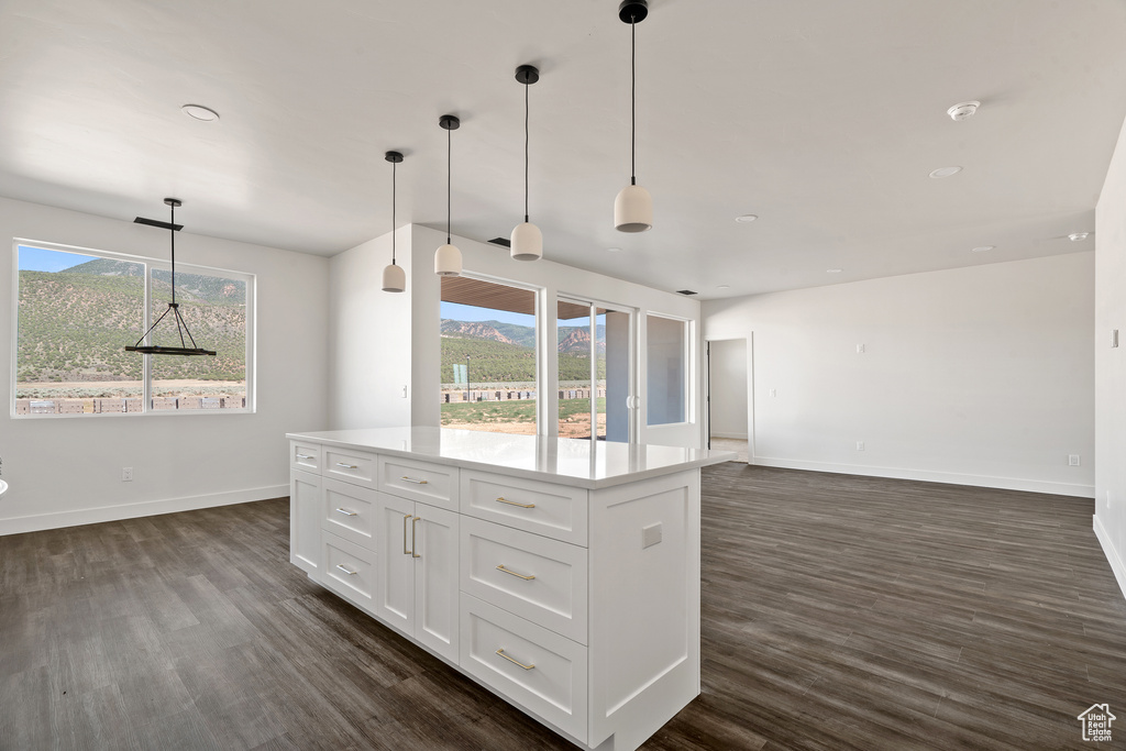 Kitchen with dark wood-style floors, white cabinets, light countertops, hanging light fixtures, and a kitchen island