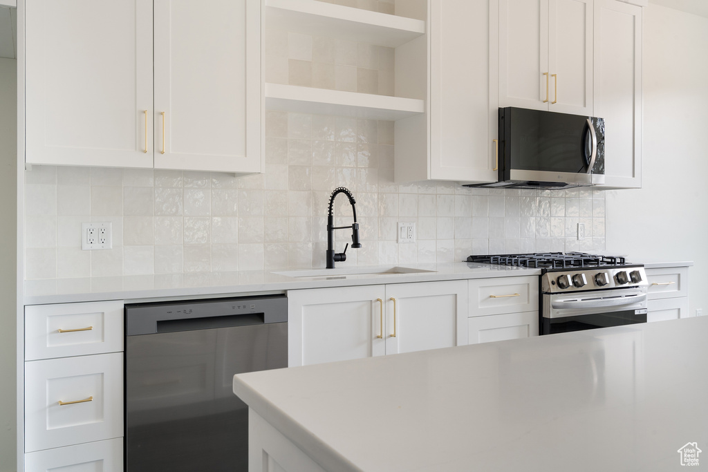 Kitchen featuring stainless steel appliances, open shelves, light countertops, and white cabinetry