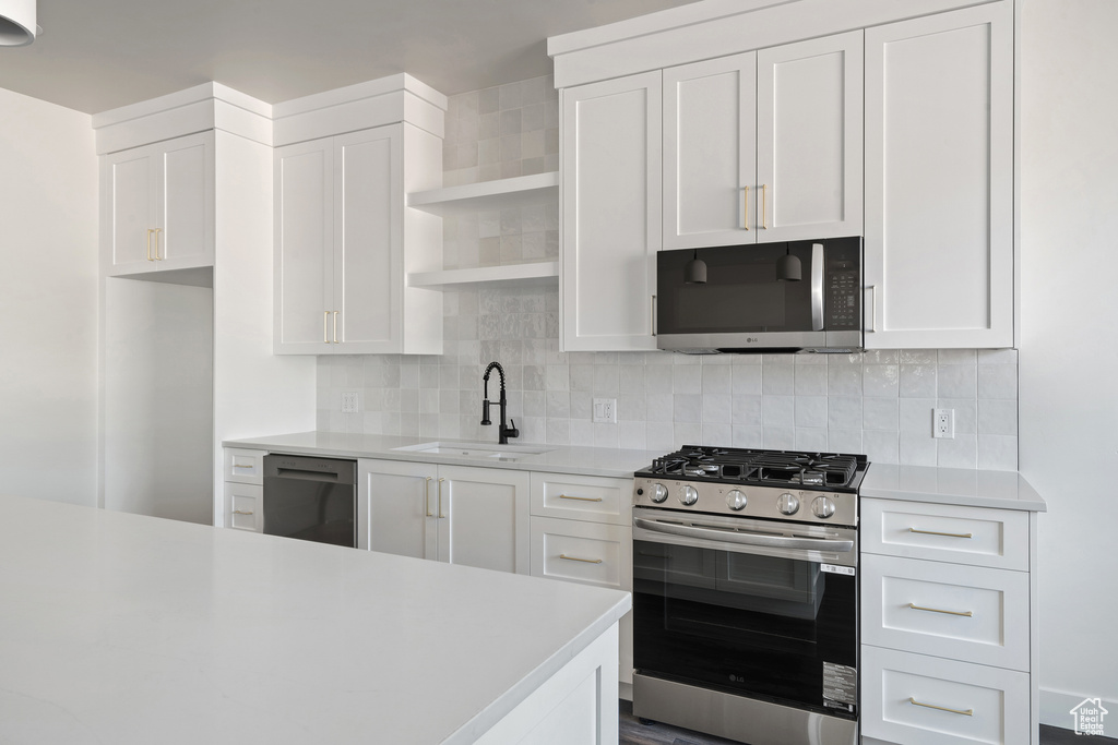 Kitchen featuring stainless steel appliances, open shelves, light countertops, and white cabinetry