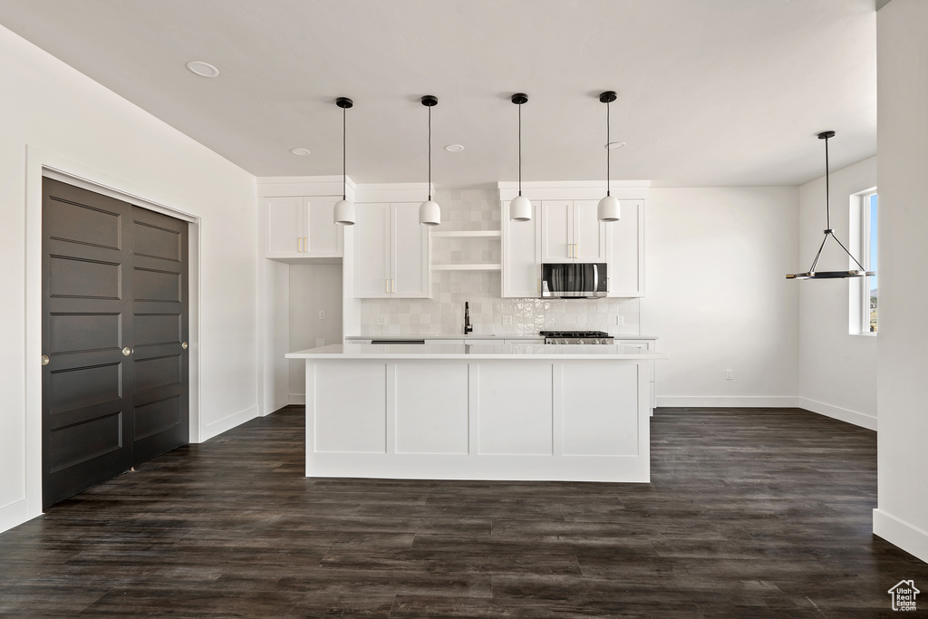 Kitchen featuring stainless steel microwave, white cabinetry, decorative backsplash, light countertops, and dark wood-type flooring