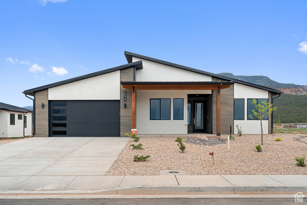 Modern home with a garage, concrete driveway, a mountain view, and stucco siding