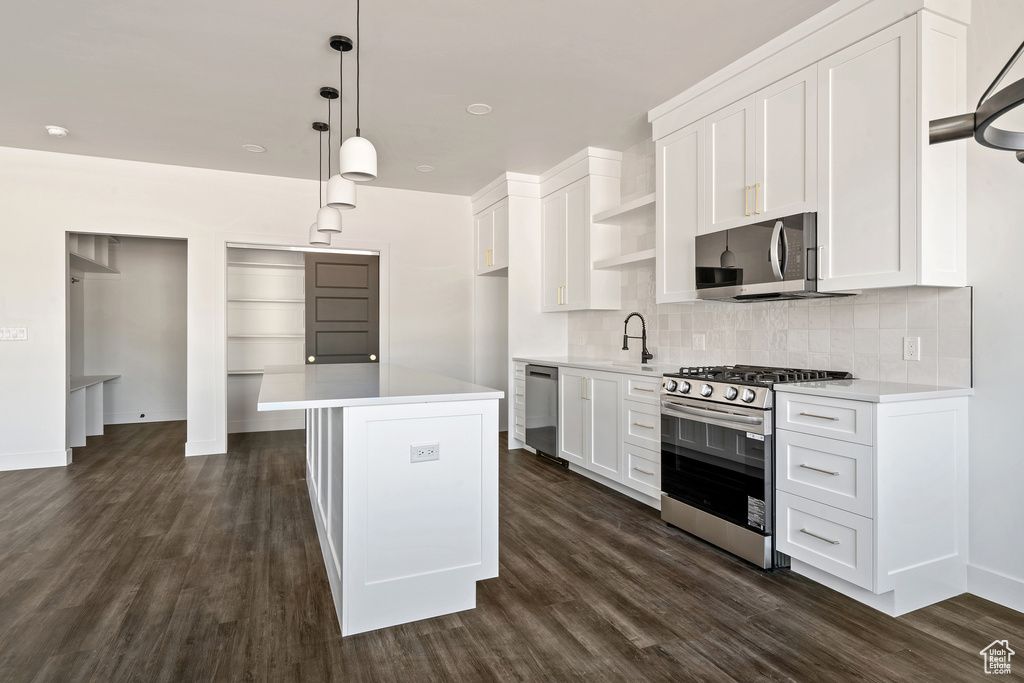 Kitchen featuring appliances with stainless steel finishes, open shelves, light countertops, and decorative backsplash