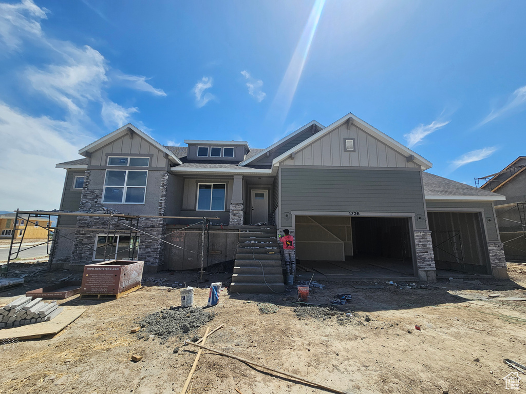 View of front of home featuring an attached garage, board and batten siding, stone siding, and driveway