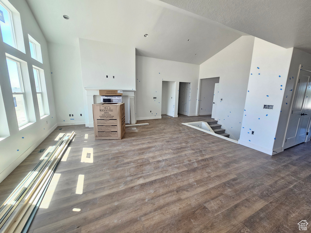 Unfurnished living room featuring high vaulted ceiling, wood finished floors, and stairway
