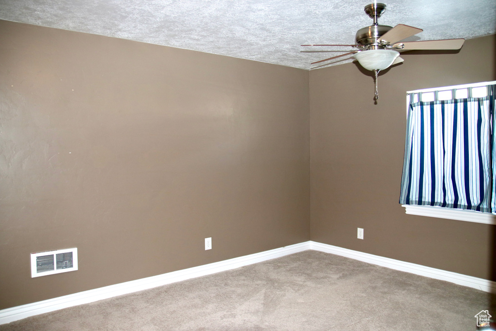 Empty room featuring a ceiling fan, carpet, and a textured ceiling