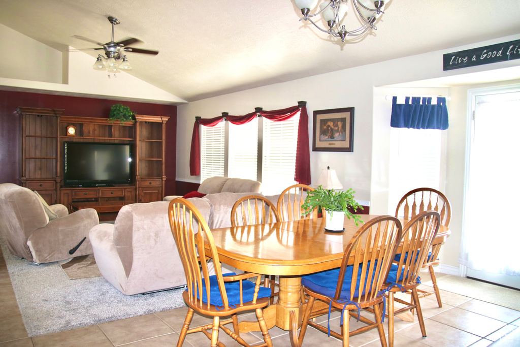 Dining room featuring a chandelier, vaulted ceiling, light tile patterned floors, and ceiling fan