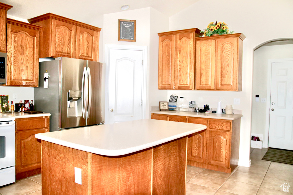Kitchen with appliances with stainless steel finishes, light tile patterned floors, light countertops, a center island, and arched walkways