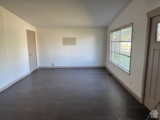 Unfurnished room featuring vaulted ceiling, dark wood-style flooring, and a textured ceiling