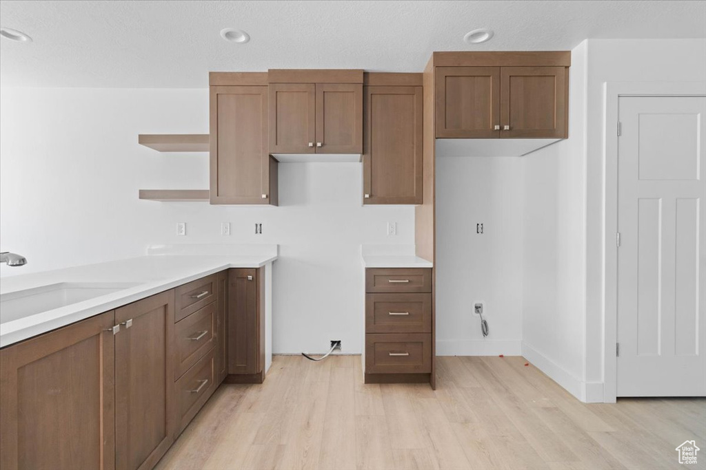 Kitchen featuring light wood-style flooring, open shelves, light countertops, and brown cabinetry