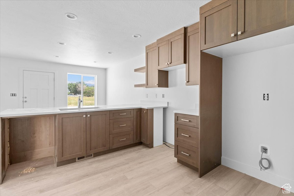 Kitchen featuring light wood finished floors, a peninsula, light countertops, brown cabinets, and recessed lighting