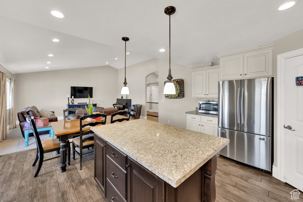 Kitchen with appliances with stainless steel finishes, vaulted ceiling, arched walkways, light wood-type flooring, and open floor plan