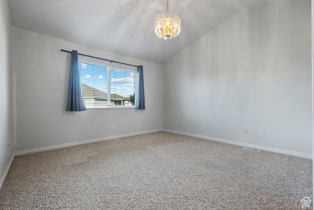 Carpeted empty room with a chandelier and lofted ceiling