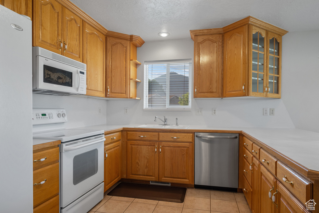 Kitchen featuring white appliances, glass insert cabinets, brown cabinets, and a textured ceiling
