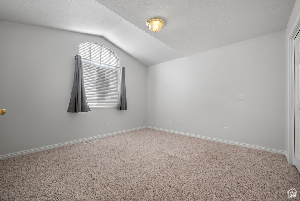 Unfurnished room featuring vaulted ceiling and carpet