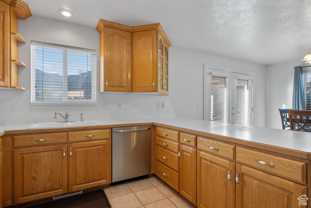 Kitchen with stainless steel dishwasher, a peninsula, light countertops, light tile patterned flooring, and glass insert cabinets